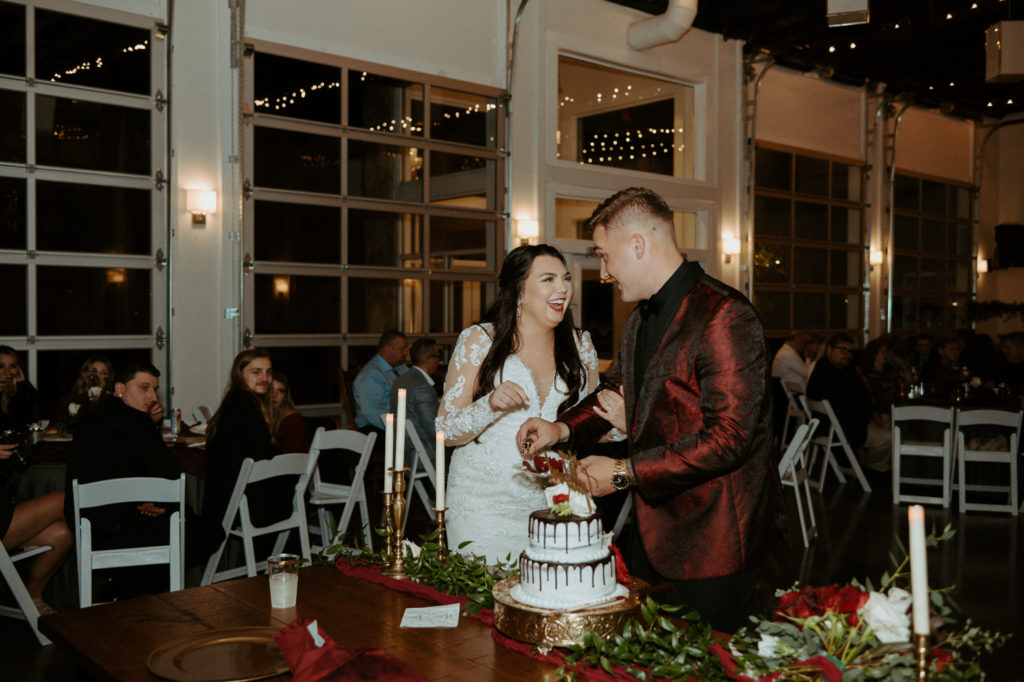 Shelby and Jacob cutting their wedding cake during their reception at The Ruby Cora surrounded by their family and friends. 