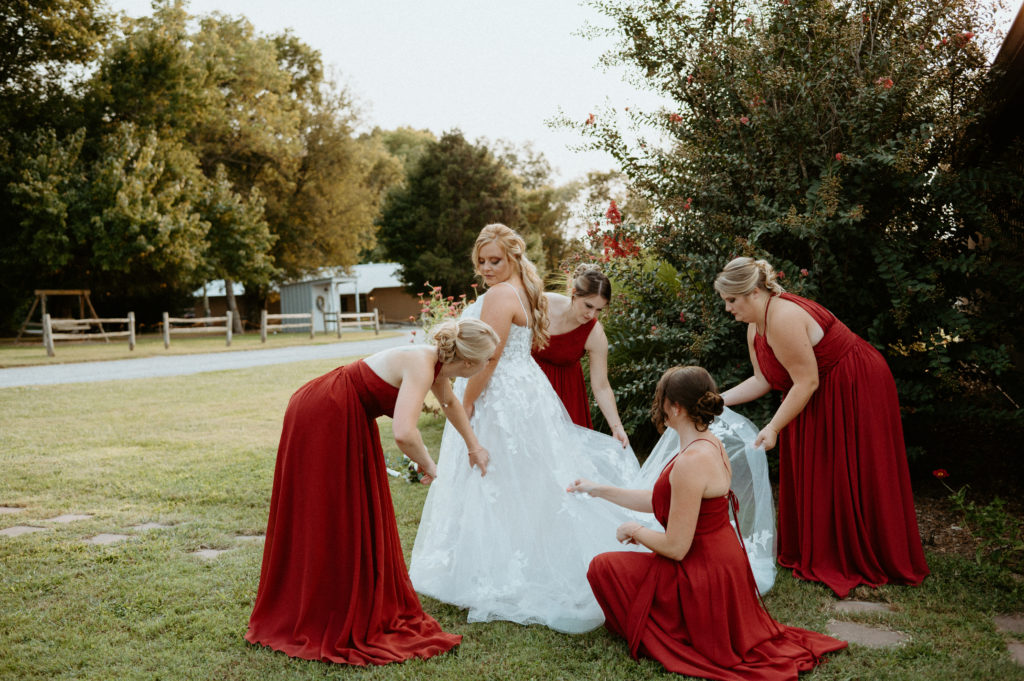 Kayla's bridesmaids helping her fluff her dress for photos during her wedding day. 
