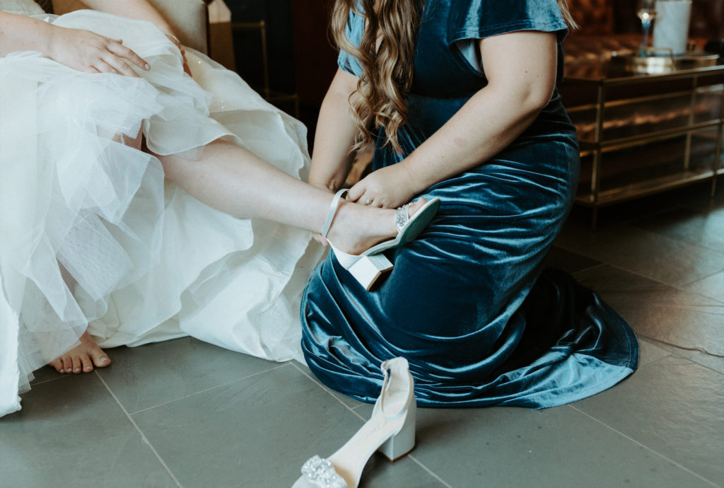 Marissa's sister helping her put on her heels while she was getting ready on her wedding day. 
