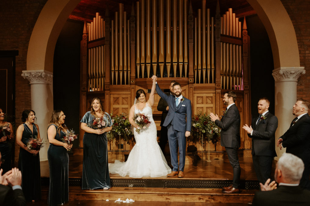 Ryan and Marissa standing in front of the organ at Clementine Hall during their fall wedding. 