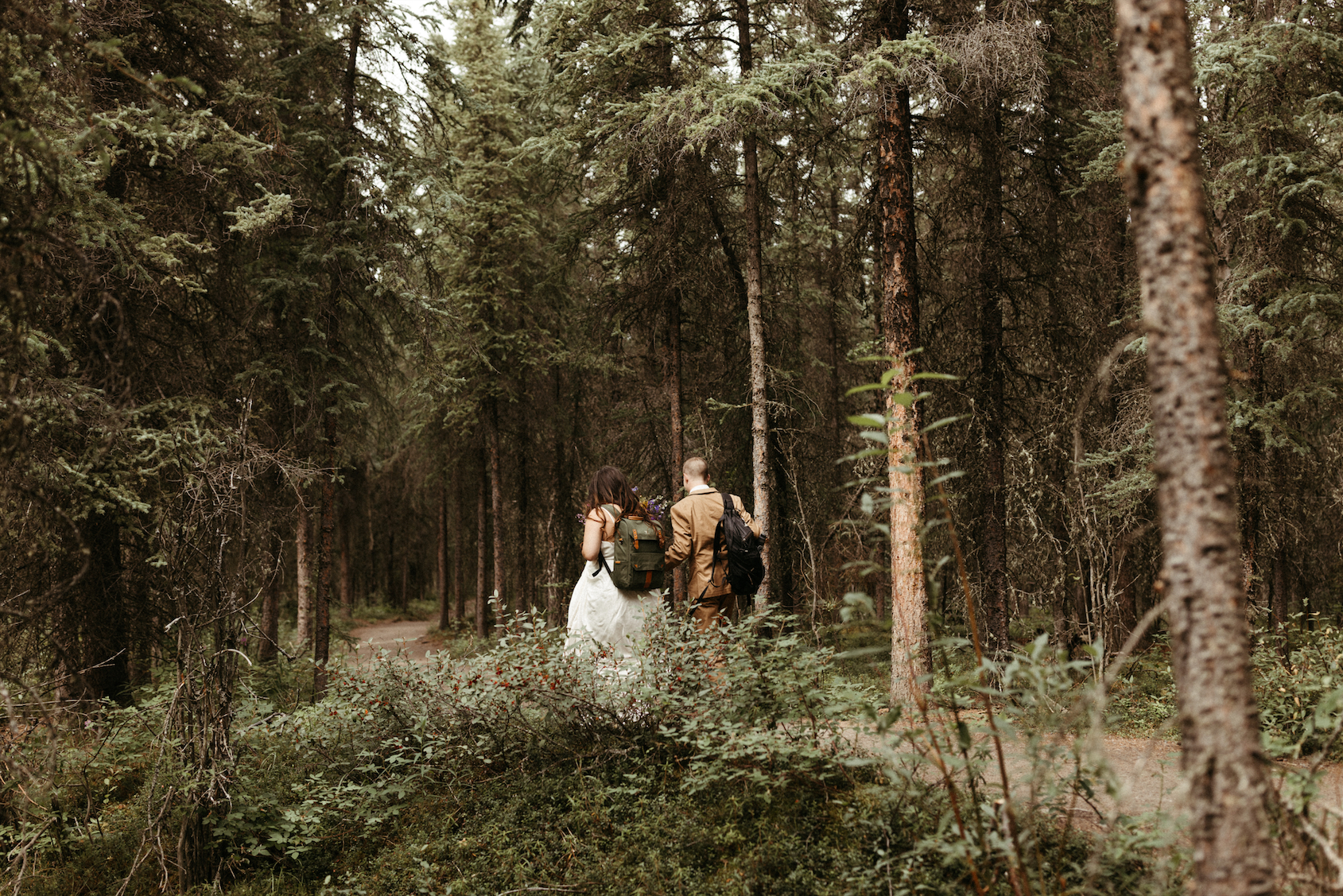 Couple walking in wedding attire through the woods.