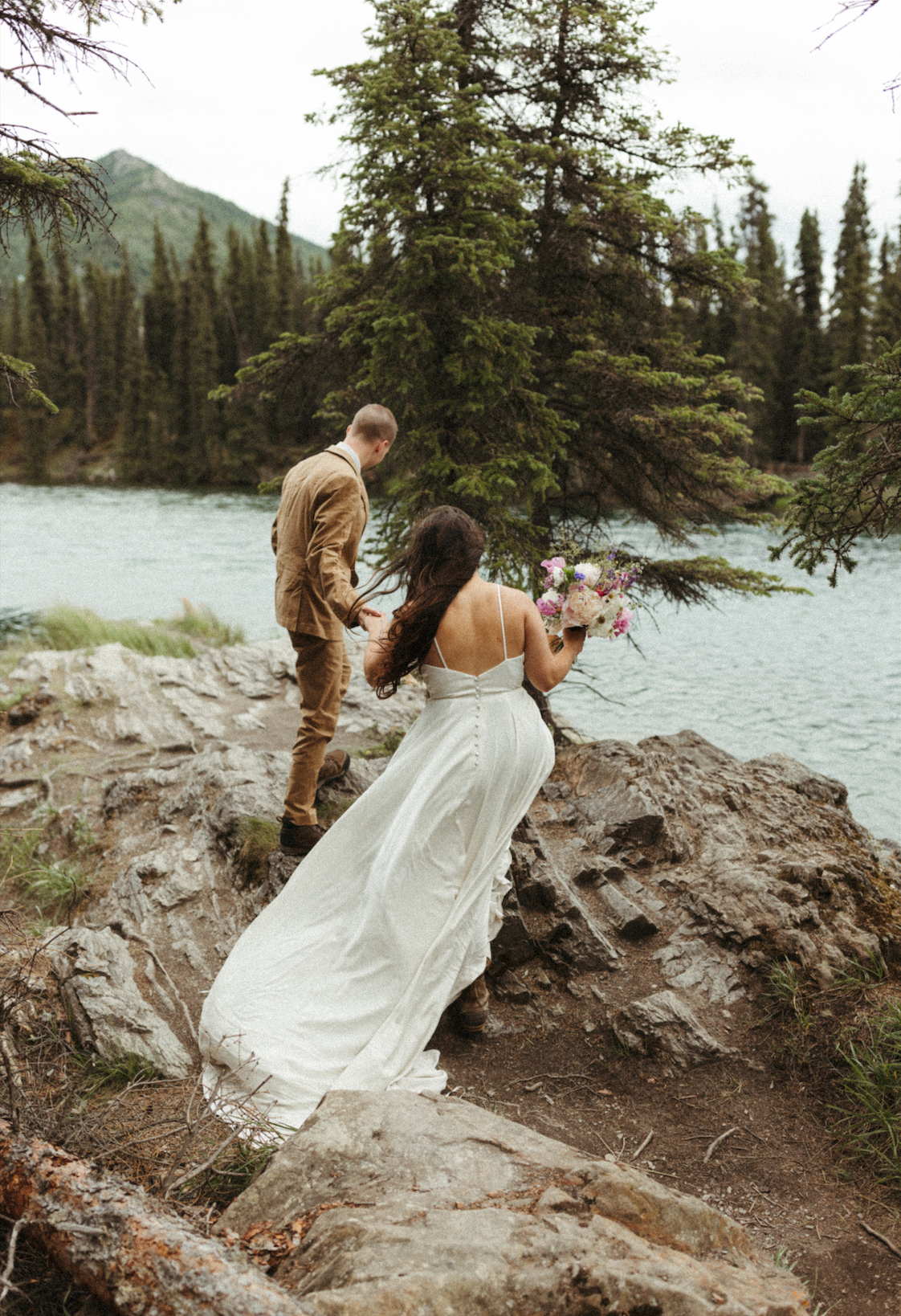 Groom helping bride onto a rock during their elopement in Denali National Park