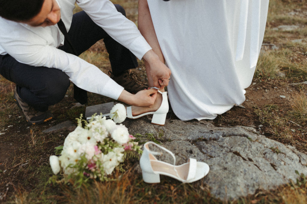 Man helping his bride put on her shoes during her Alaska wedding