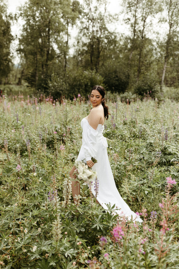 Woman looking down her shoulder in a field of flowers after hair and makeup.
