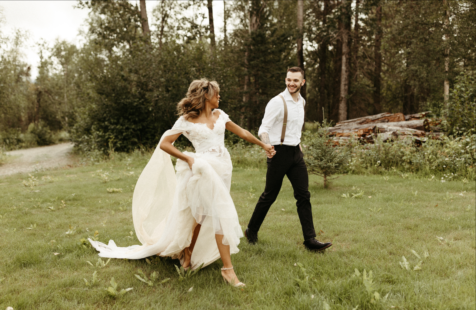 Bride and groom holding hands and running through a field of grass during springtime in Alaska. 
