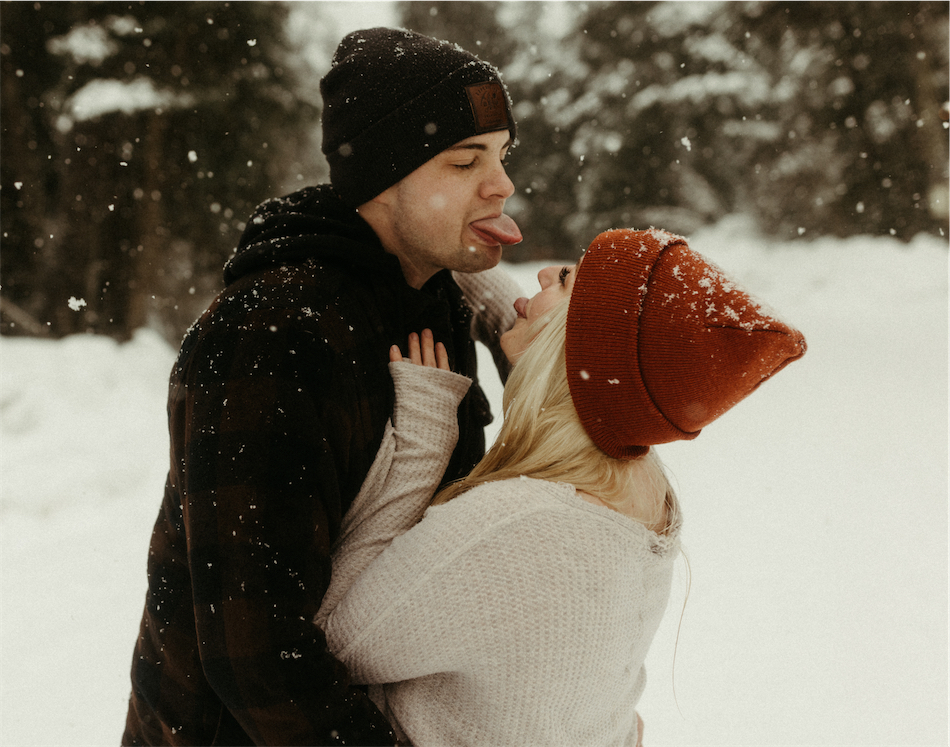 Couple sticking their tounges out at one another and catching snowflakes 