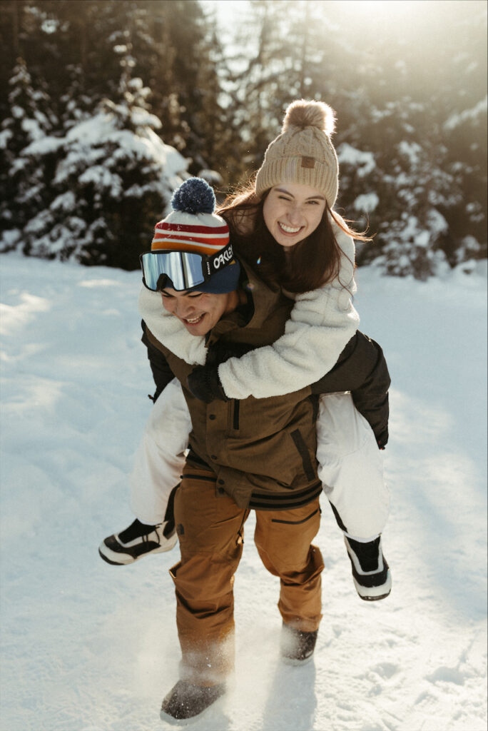 Couple piggybacking in the snow during the adventure engagement session in Girdwood, Alaska