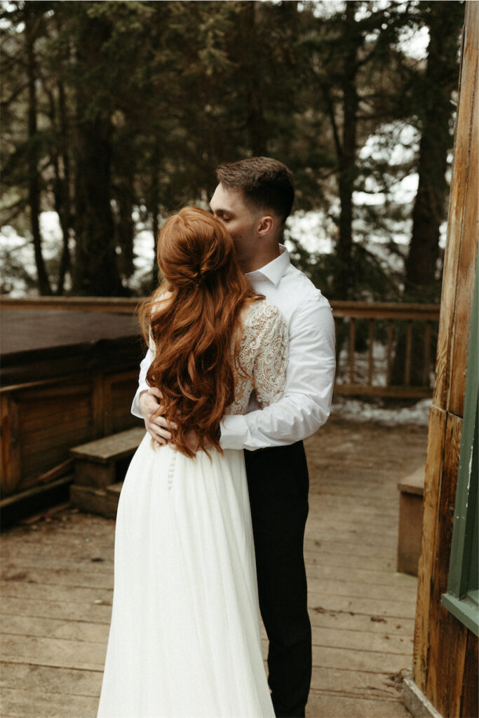 Man and woman hugging one another outside their a frame cabin 