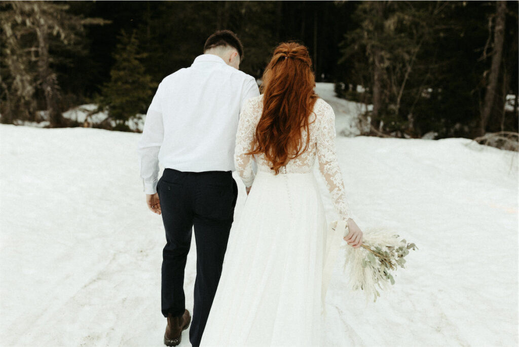 Man and woman walking into the woods in elopement attire in Girdwood, Alaksa