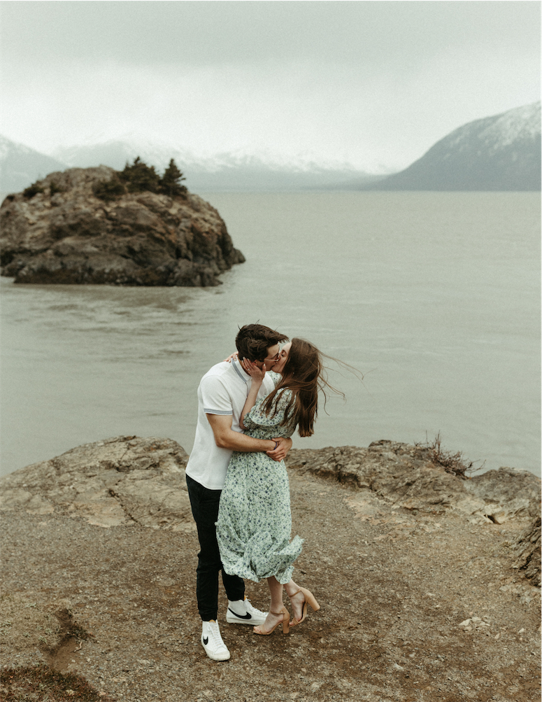 Couple snuggled close and kissing on top of a rock in Anchorage, Alaska during their engagement session 