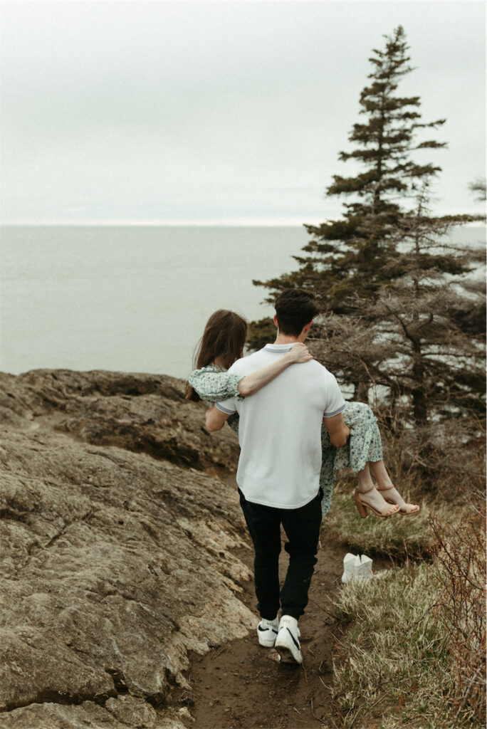 Man carrying woman down the rocks at Beluga point during their couples photoshoot