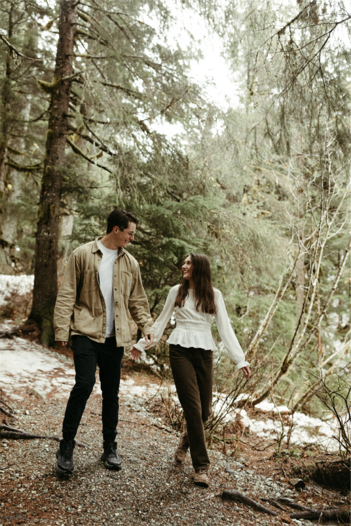 Couple holding hands and walking through the woods in Girdwood during their couples photoshoot