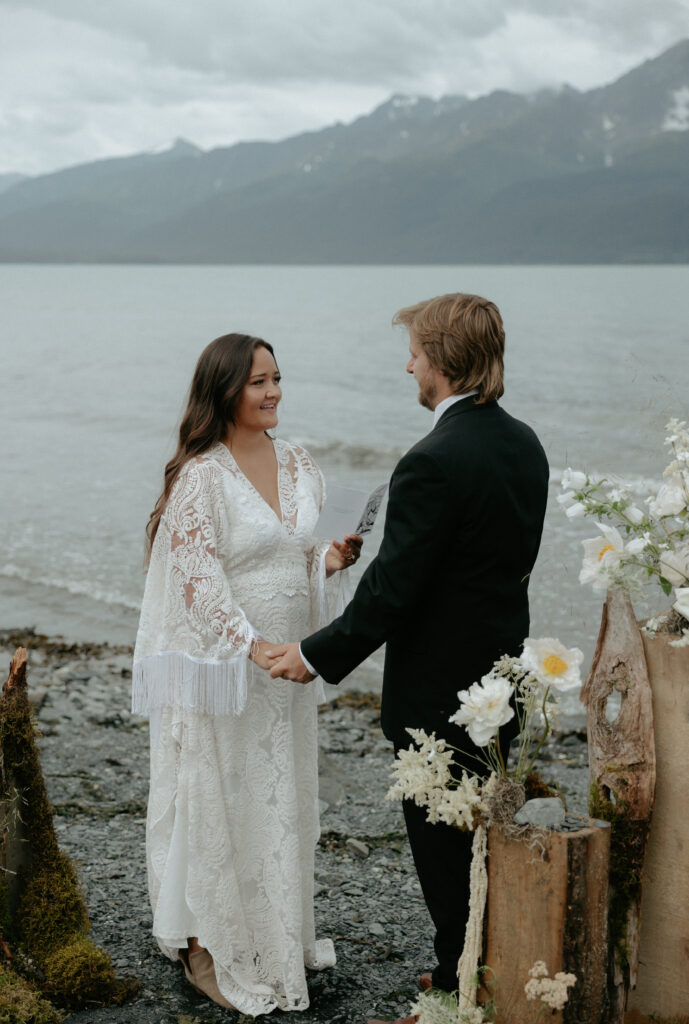 A man and woman holding hands while standing next to the ocean. 