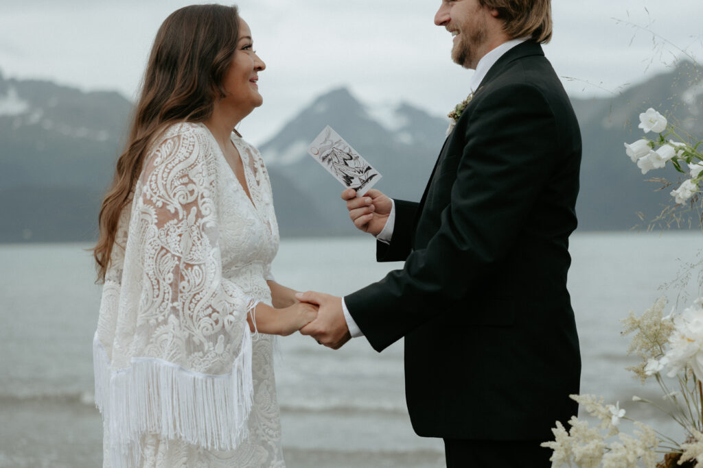 A man and woman smiling at one another as they read vows. 