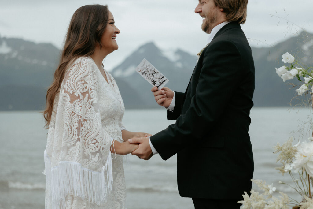 A couple holding hands and looking at one another while standing on a beach. 