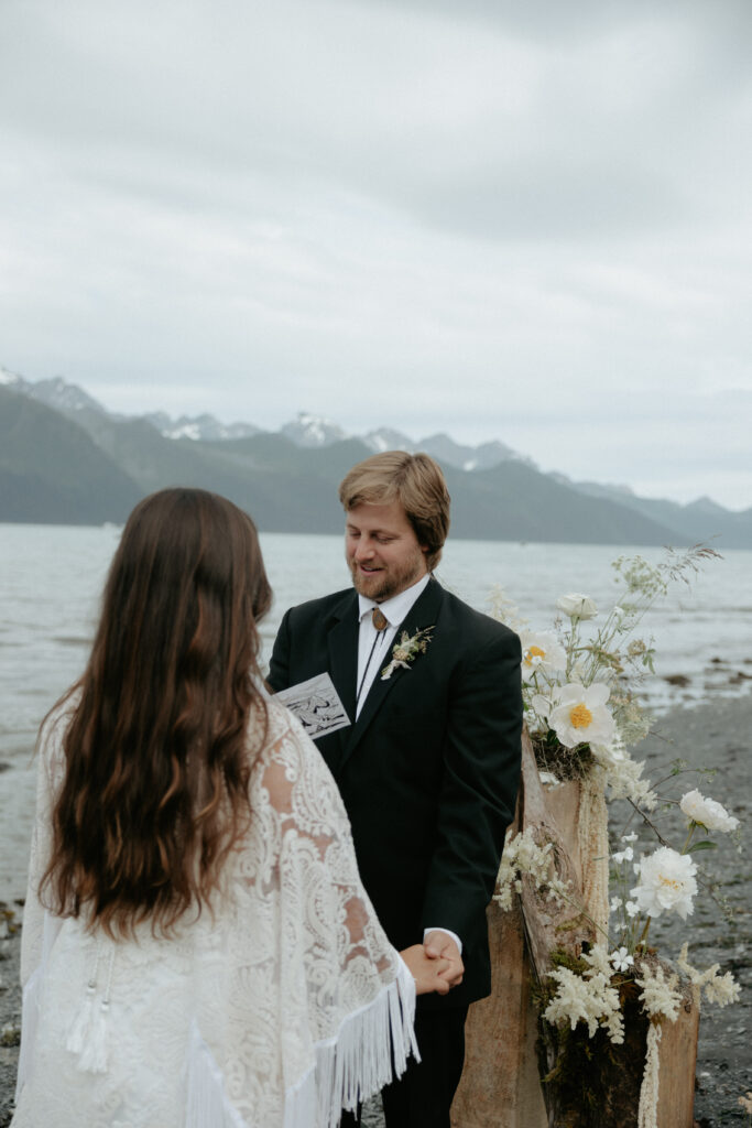 A man wearing a black suit holding a woman's hand as he looks down at a white book. 