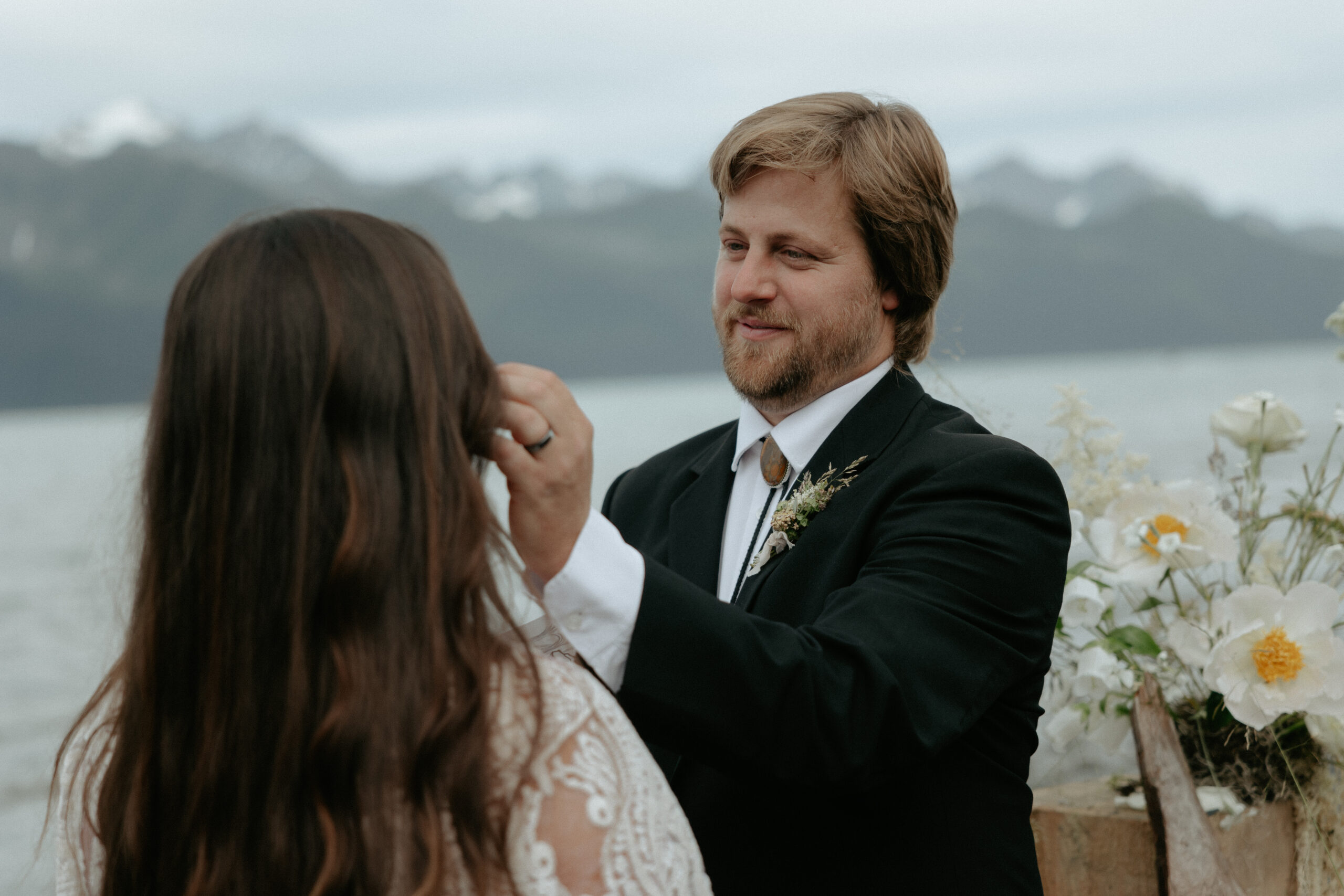 A man moving a piece of hair away from a woman's face during a wedding ceremony.
