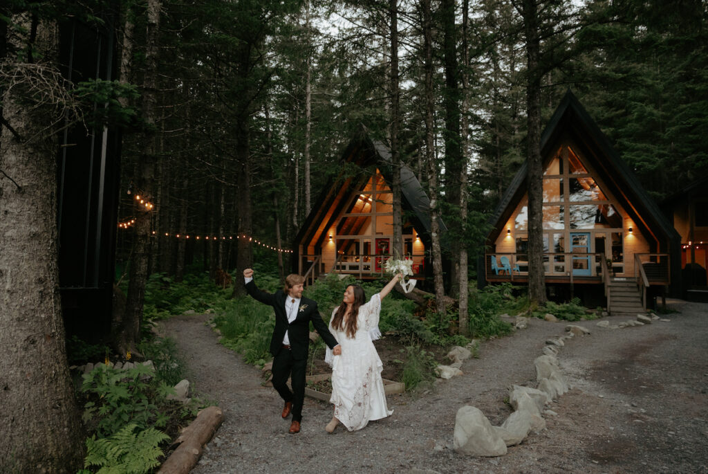 A couple holding hands and walking away from a lit up a-frame cabin.