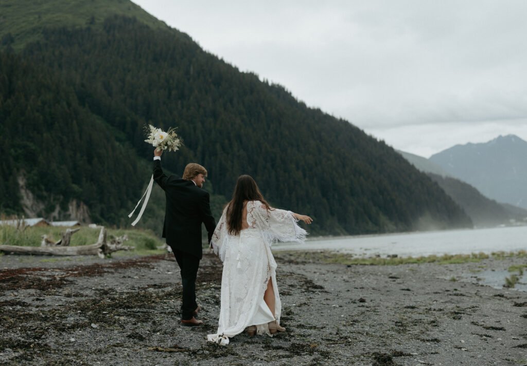 A couple holding hands and walking down the shoreline. 