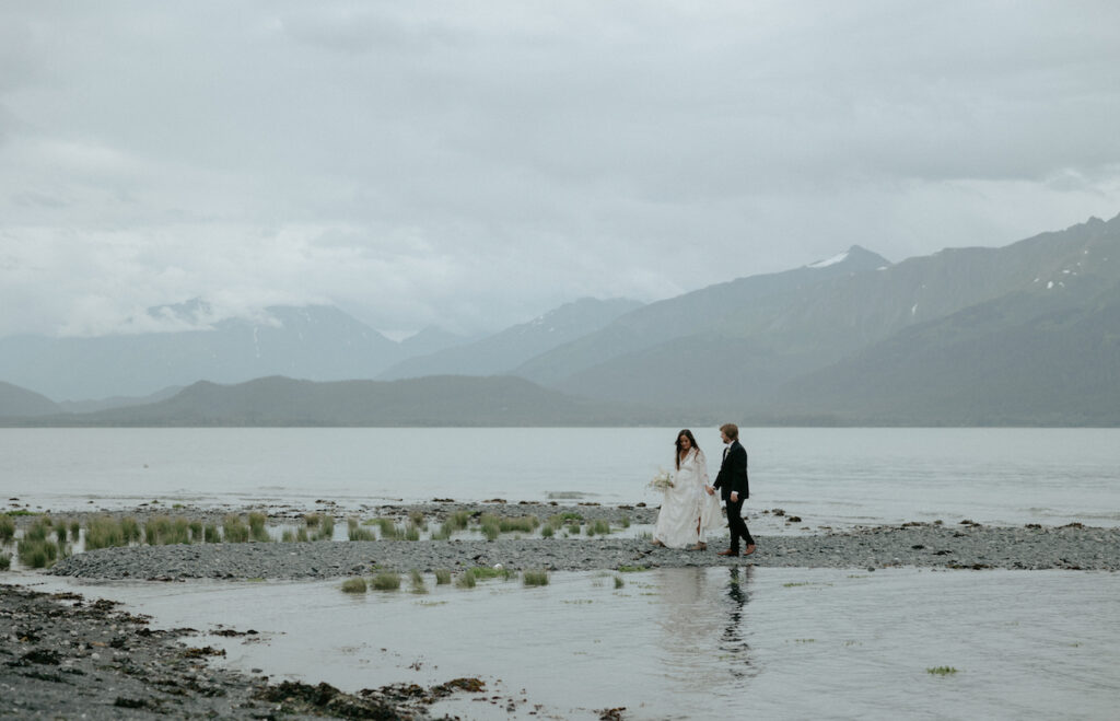 A couple walking on the beach with the mountains behind them. 