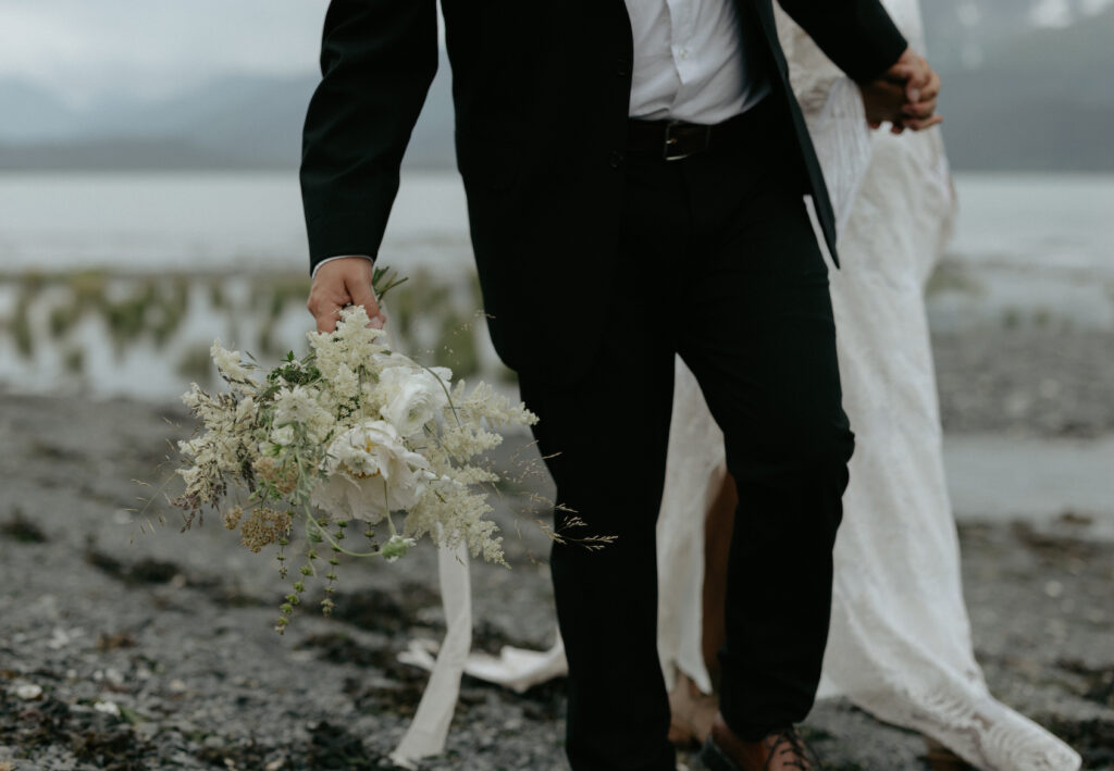 A man wearing a black suit carrying a bouquet of white florals. 