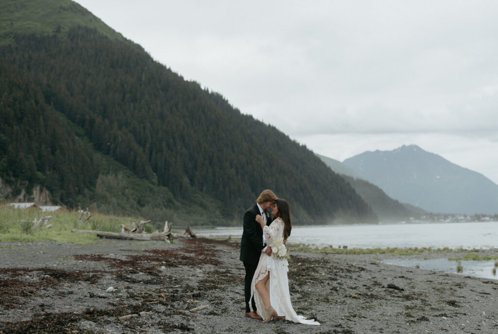 A couple embracing one another on the beach with seaweed on the ground around them. 