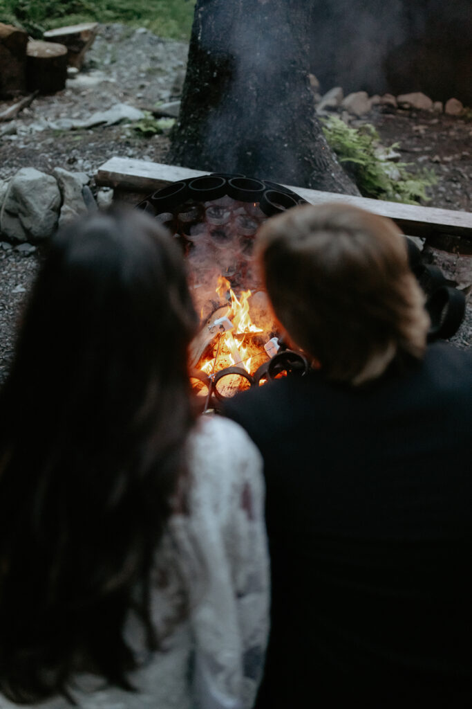 A couple sitting by a fire and roasting marshmellows. 