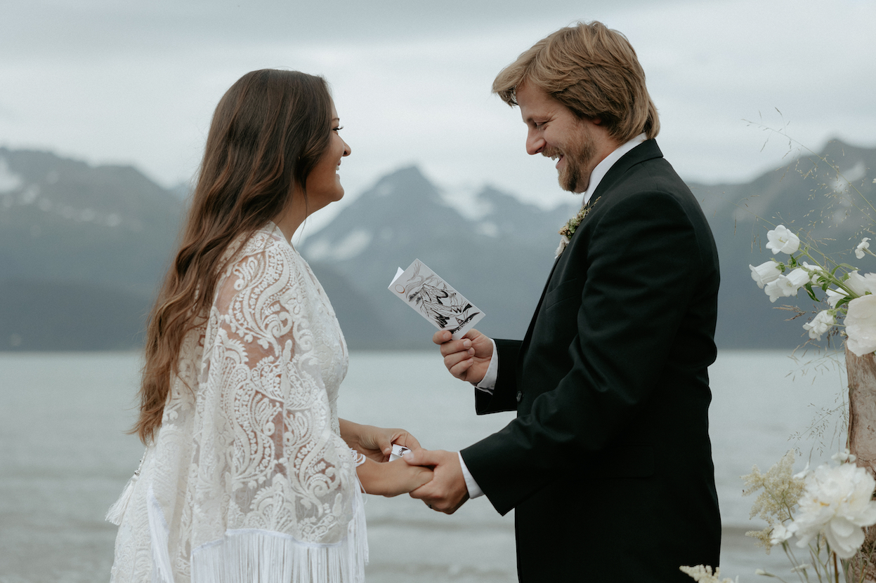 A couple reading vows to one another on a beach in Alaska