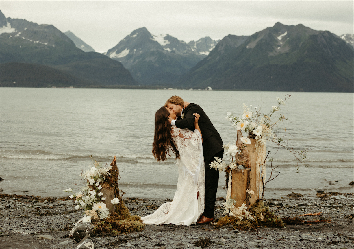 Couple kissing on the beach standing next to mountains in Alaska