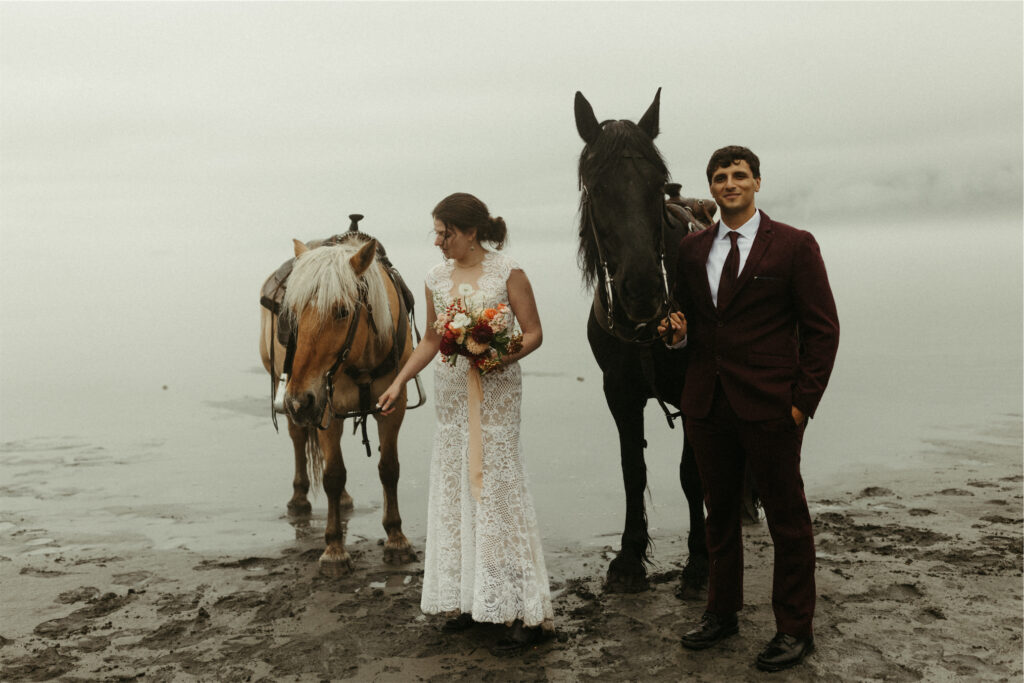 Couple standing on the beach with horses during their elopement in Alaska