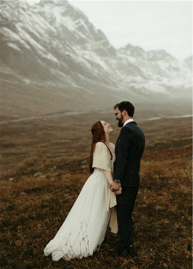 Couple holding hands and smiling as the snow falls during their Hatchers Pass elopement