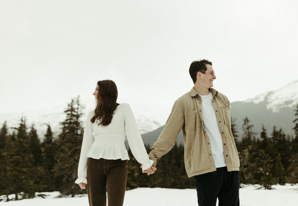 Couple standing next to mountains while taking photos in Alaska