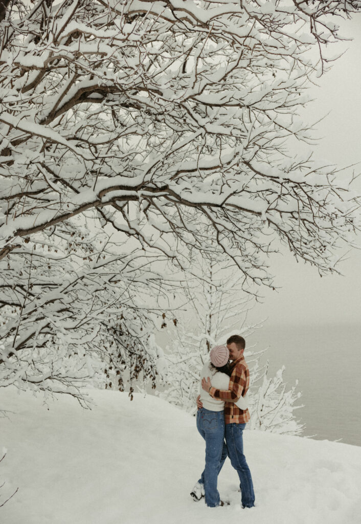 Couple snuggled up close under a tree during their outdoor proposal