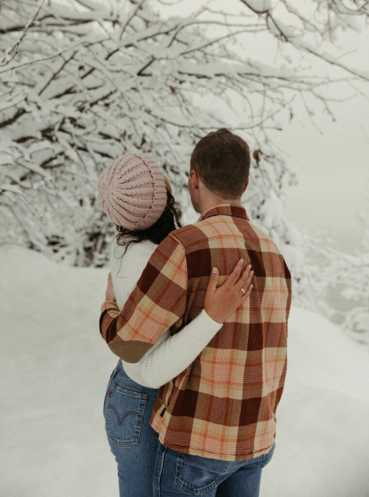 Couple looking up at the snow on the trees during their winter engagement session