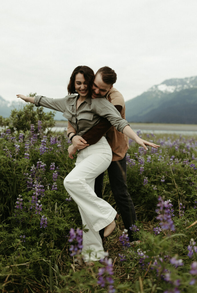 Couple playing airplane with one another in a field of lupines in Alaska 