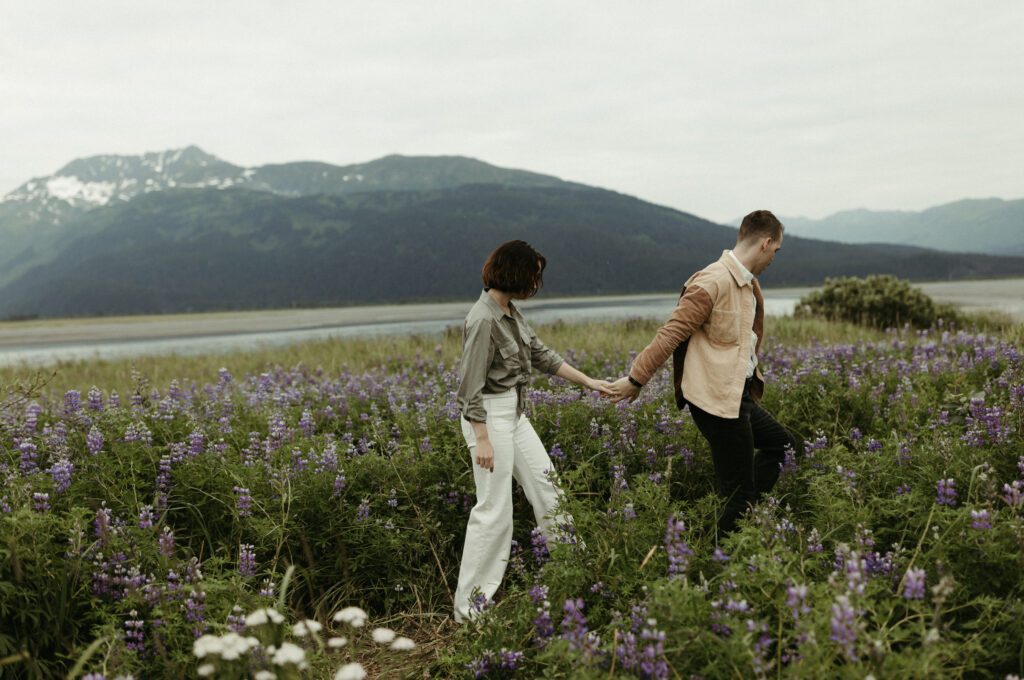 Man leading woman in a field of lupines during their engagement photo shoot in Alaska 