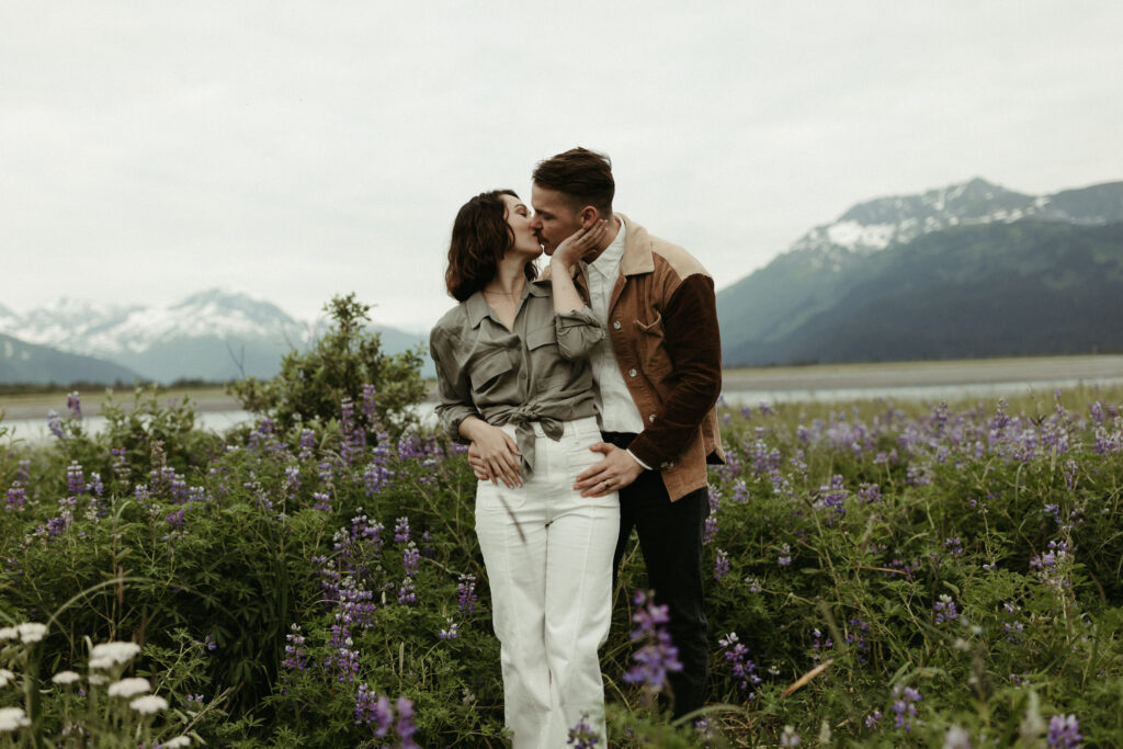 Couple kissing while in a field of lupines next to the ocean.