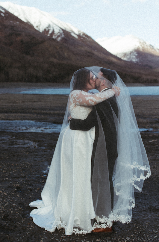 Couple kissing while standing next to the mountains at Eklutna Lake