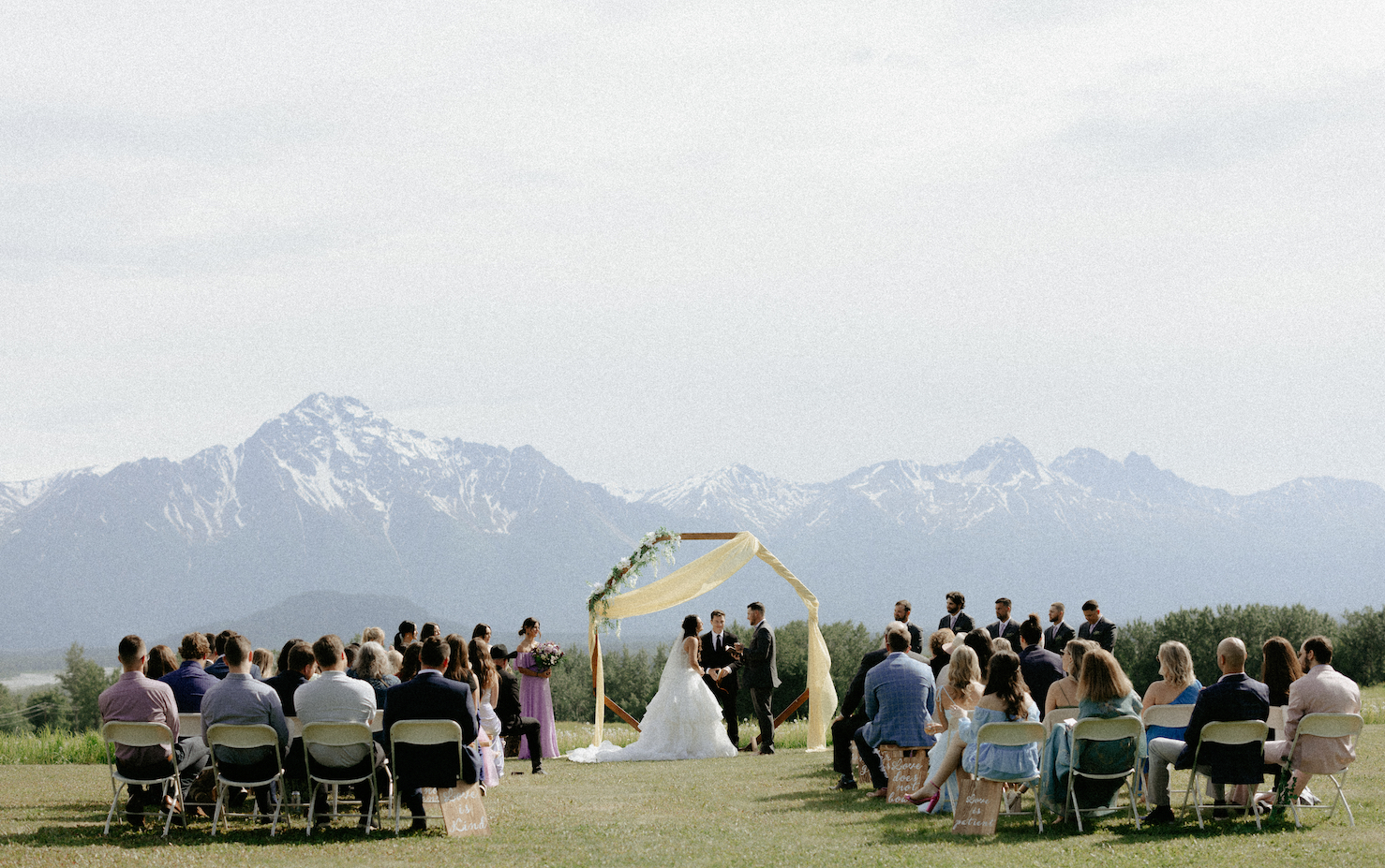 A couple holding hands in front of an arch overlooking the mountains.