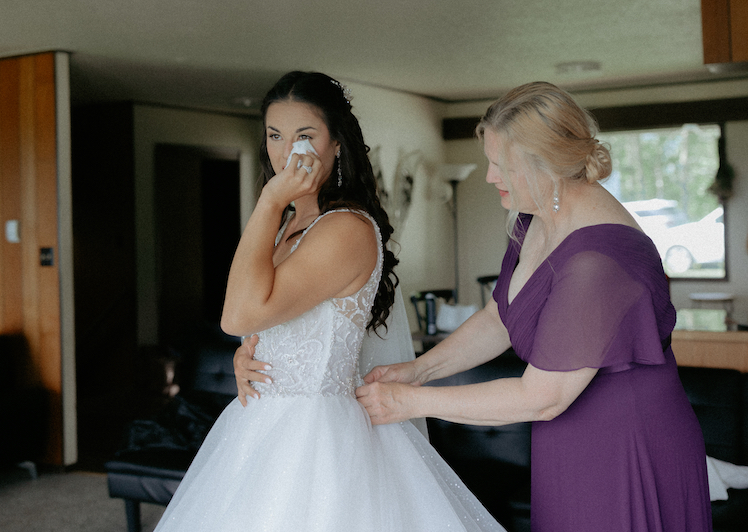 A woman zipping up a brides dress during her Alaska wedding.