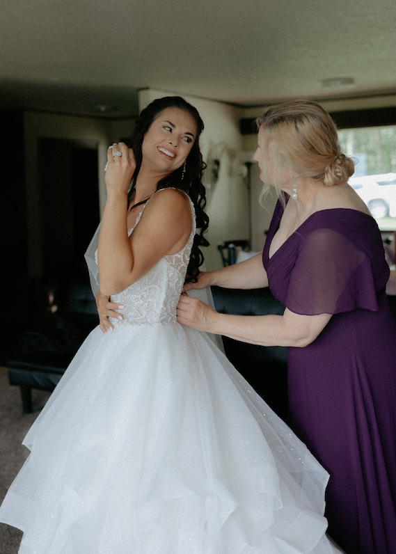 Daughter looking back at her mother as she zips her wedding dress.