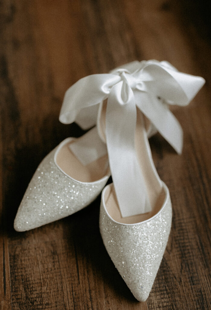 A pair of white wedding shoes sitting on a dark wood floor.