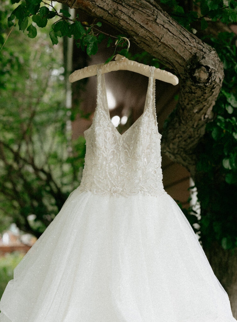 A white wedding dress hanging from a tree covered in white flowers.