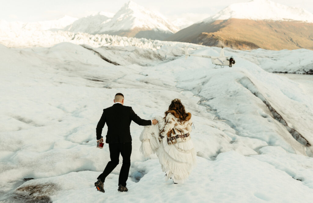 Man holding womans dress as they walk toward a glacier