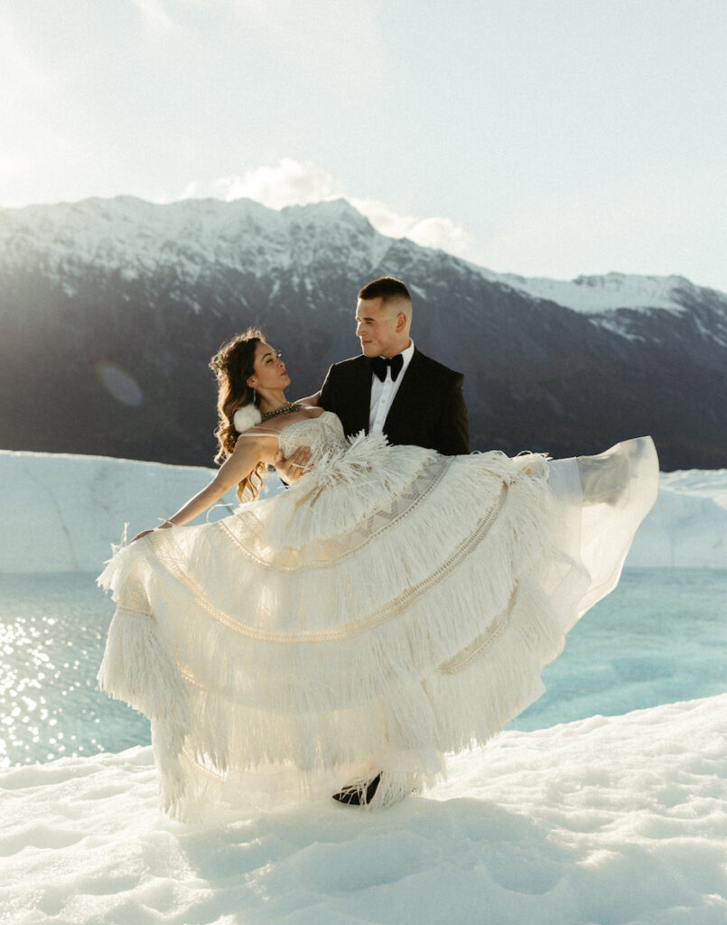 Man picking up a woman who is wearing a white dress