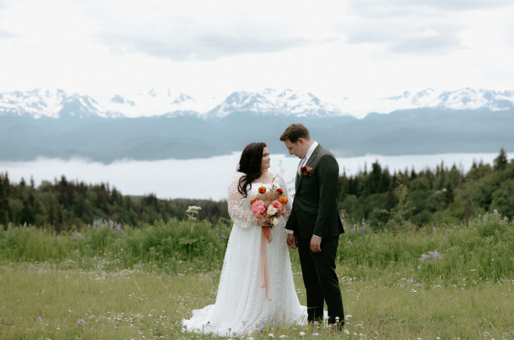 Couple standing in a field next to an overlook in Homer, Alaska.