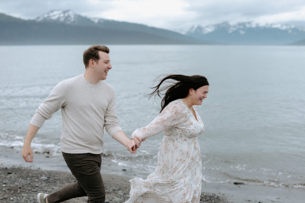 Man and woman laughing together while running along the beach shore