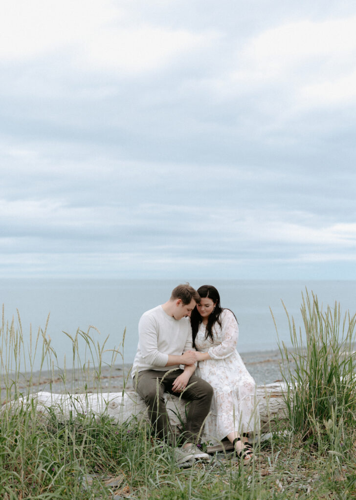 Couple snuggled up to one another while sitting on a log on the beach