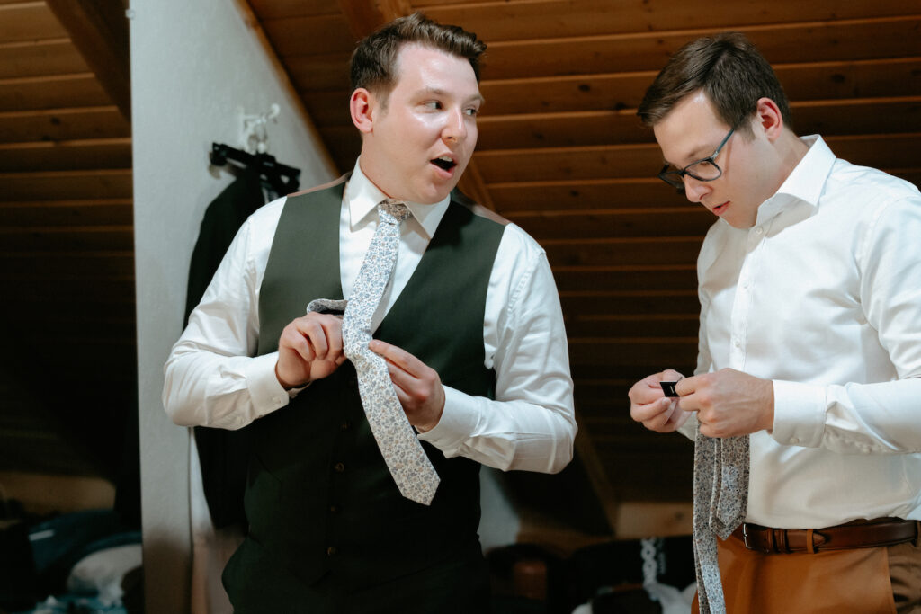 Groom tying his tie while getting ready with his brother by his side.