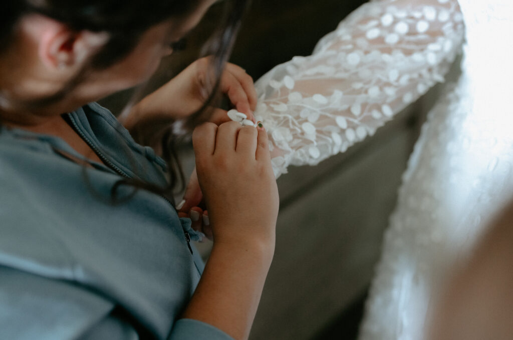 Friend of the bride buttoning the sleeves on her wedding dress.